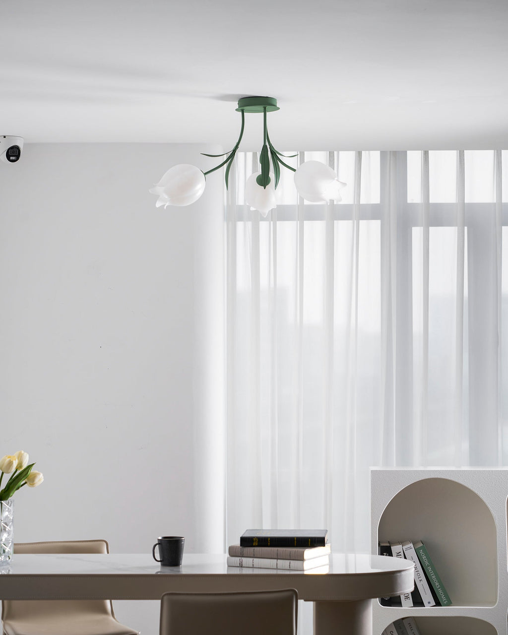 Lit above a dining table, this Clérachic ceiling light in green hangs near sheer curtains and a bookshelf.
