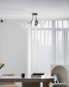Lit above a dining table, this Clérachic ceiling light in green hangs near sheer curtains and a bookshelf.