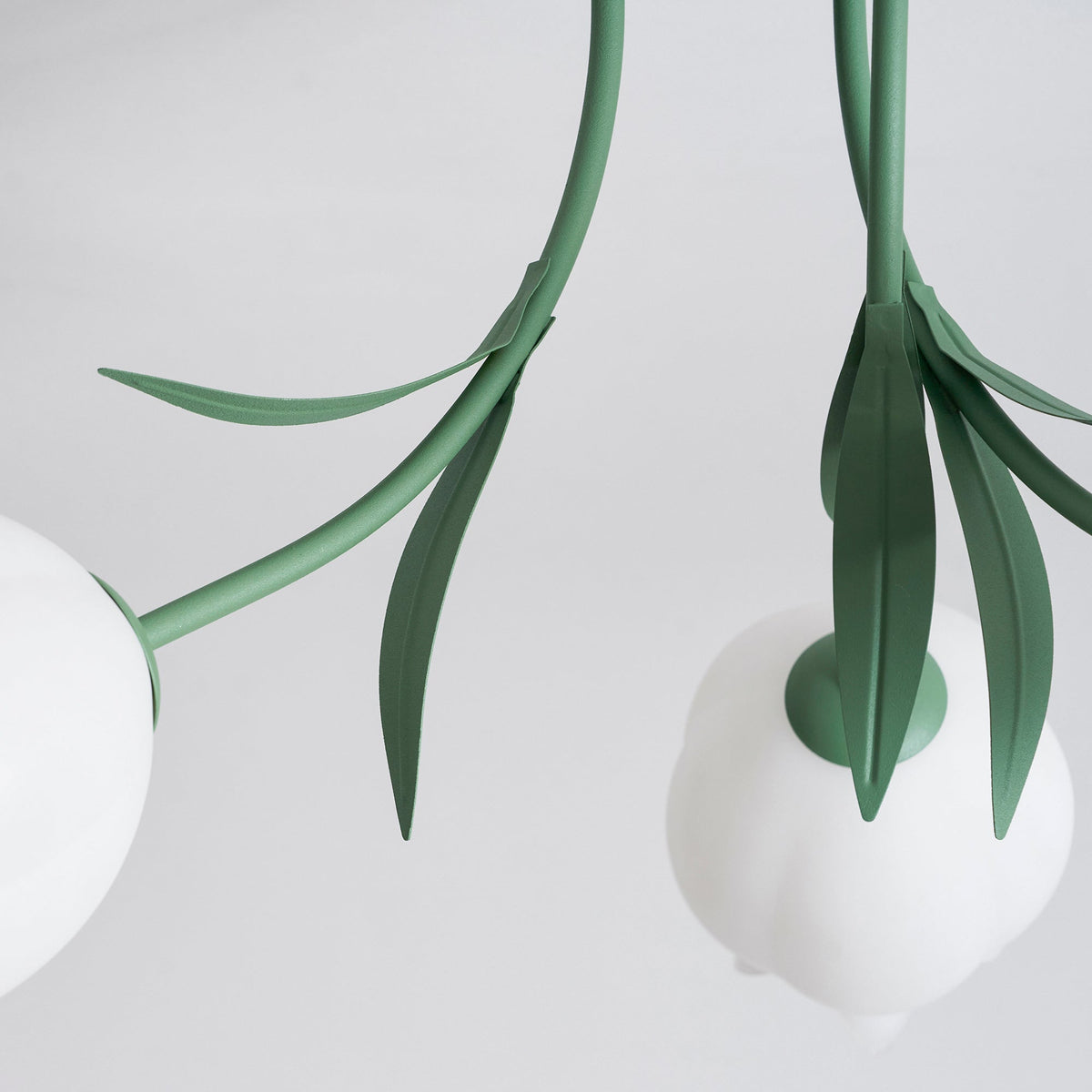 Close view of two stems and leaves on this Clérachic ceiling light in green, converging near the ceiling mount.