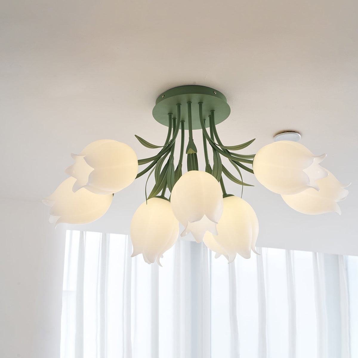 Glowing warm from below near a sheer curtain, this Clérachic ceiling light in green lights the cluster of shades.