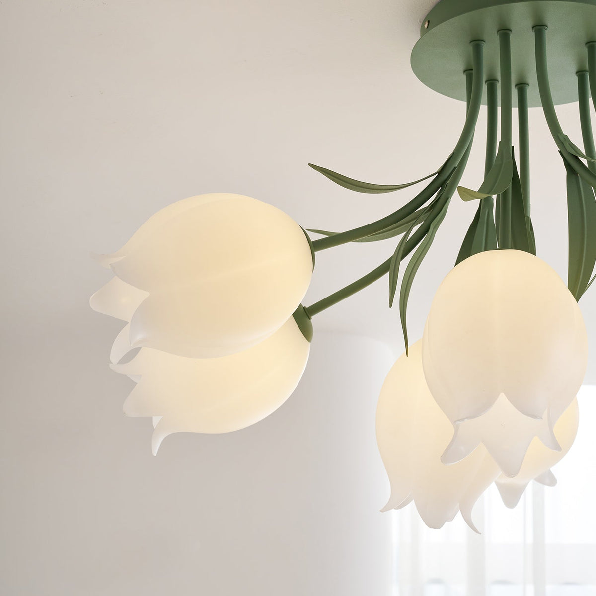 Close view of the green stems and leaves fanning from the ceiling mount on this Clérachic ceiling light.