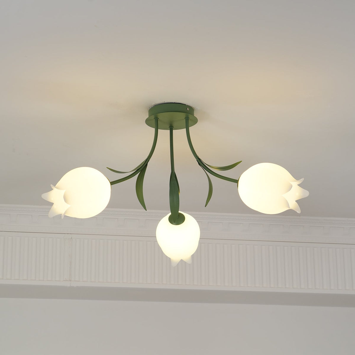 Beneath a decorative cove moulding, this Clérachic ceiling light in green hangs with its three shades unlit in daylight.