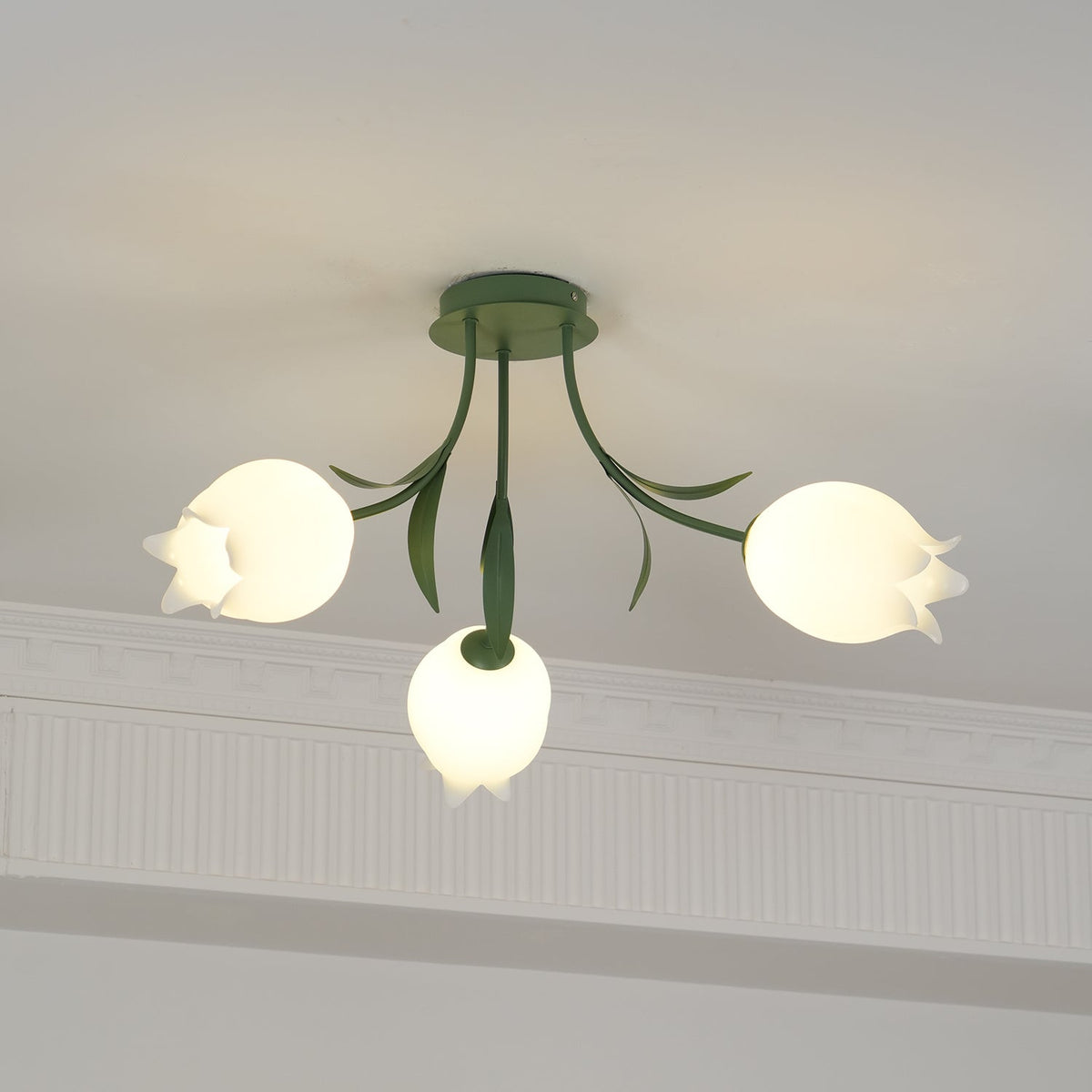 Beneath a cove moulding, this Clérachic ceiling light in green glows softly, its three shades lit warm.