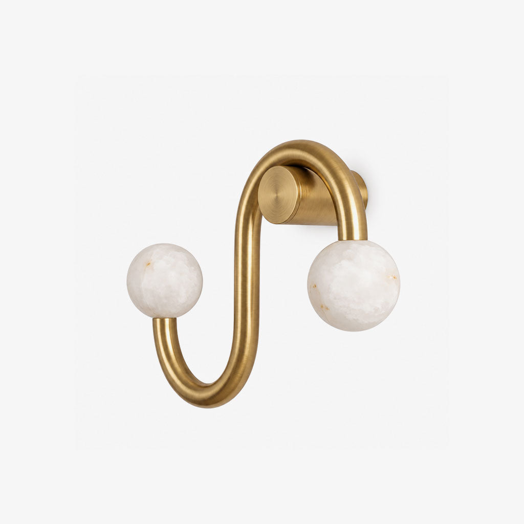 Photographed on white, the brass finish of this Clérachic sconce loops into an S-shape ending in two alabaster globes.