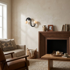 Beside a wood-framed fireplace and an upholstered armchair, this Clérachic sconce's black finish glows warmly.