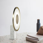 Clérachic lamp glowing on a terrazzo floor beside a dark bottle-shaped vase and a stack of books nearby.