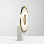 Full-length studio shot of the Clérachic gold disc table lamp lit against a plain off-white background, marble foot in view.