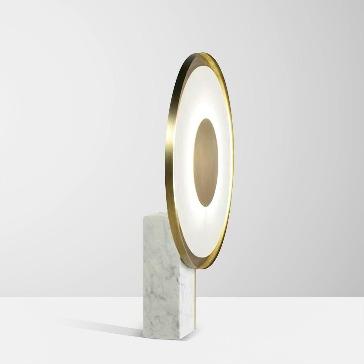 Full-length studio shot of the Clérachic gold disc table lamp lit against a plain off-white background, marble foot in view.