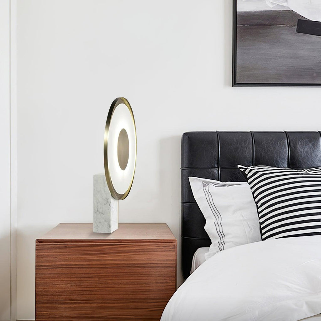 The Clérachic disc lamp sits on a dark wood bedside table next to a black leather headboard dressed with striped pillows.
