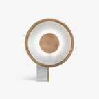 Clérachic gold disc table lamp shown straight on, lit, its rectangular marble foot planted on a plain background.