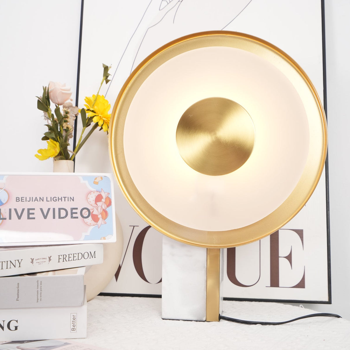 Clérachic lamp filling most of the frame beside flowers and stacked books, a line-art print and lettered card behind it.