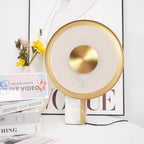 Close crop of the Clérachic lamp's frosted glass ring and gold centre disc, glowing warm against a blurred floral arrangement.
