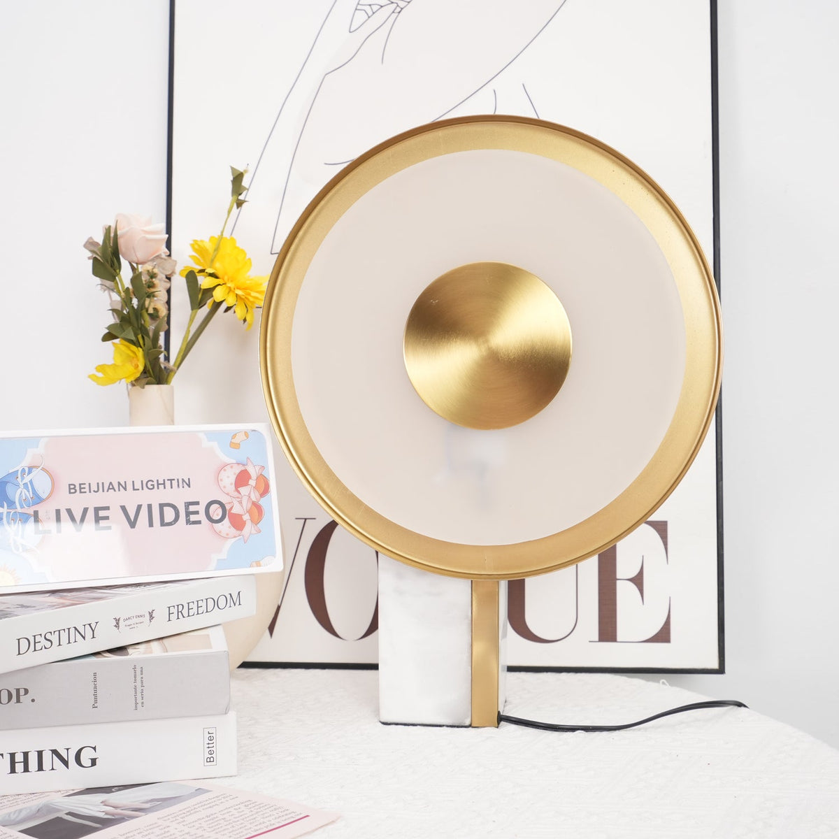Close crop of the Clérachic lamp's frosted glass ring and gold centre disc, glowing warm against a blurred floral arrangement.