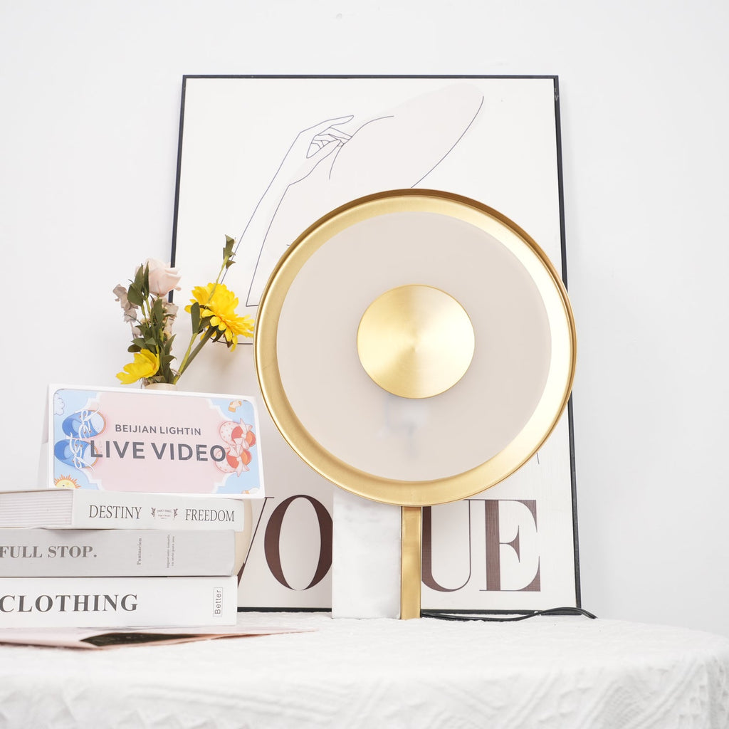 Clérachic disc lamp unlit beside a vase of yellow sunflowers and a stack of books, styled against a plain wall.