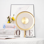 Clérachic disc lamp unlit beside a vase of yellow sunflowers and a stack of books, styled against a plain wall.
