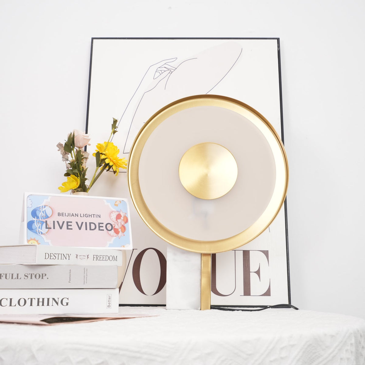 Clérachic disc lamp unlit beside a vase of yellow sunflowers and a stack of books, styled against a plain wall.