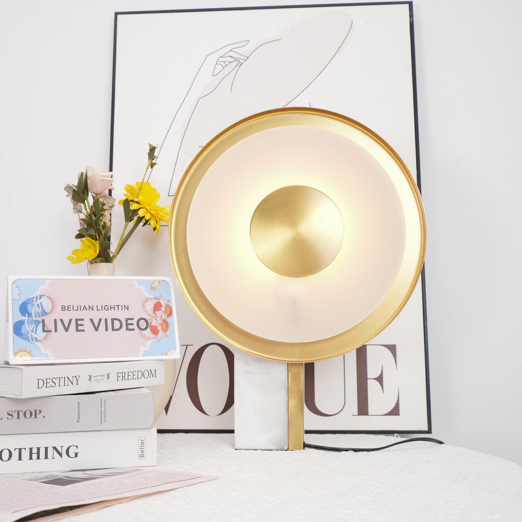 Clérachic disc lamp lit beside stacked books and flowers, a line-art figure print and lettered card visible in the background.