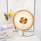 Close view of the Clérachic gold disc lamp beside a vase of pink and yellow flowers, with a stack of books at its marble base.