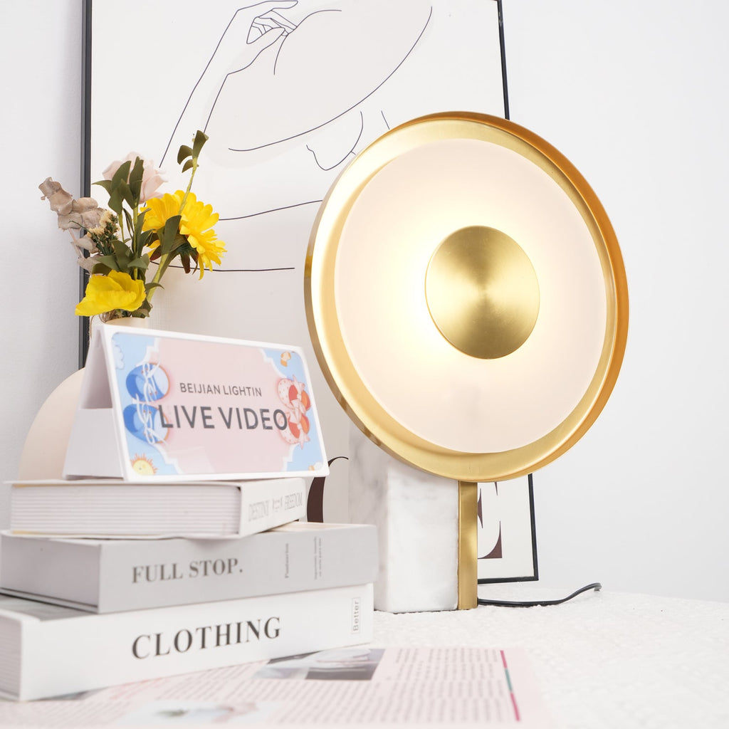 Clérachic disc lamp glowing beside yellow flowers and stacked books titled Full Stop and Clothing, a line-art print behind it.