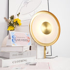 Clérachic disc lamp glowing beside yellow flowers and stacked books titled Full Stop and Clothing, a line-art print behind it.