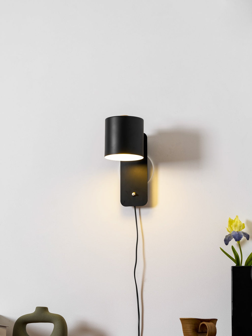 Metal cylinder wall lamp shown angled downward in an interior