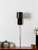 Metal cylinder wall lamp glowing gently beside a headboard