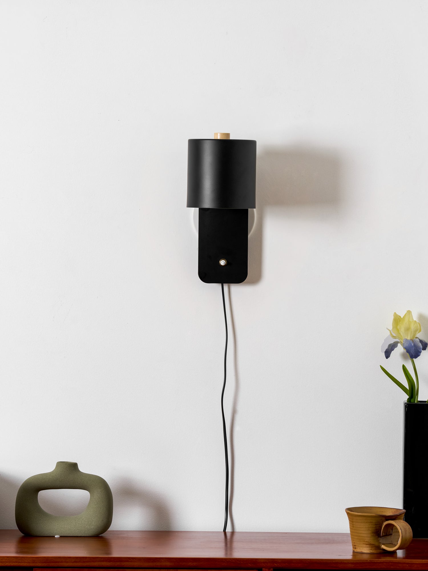 Metal cylinder wall lamp glowing gently beside a headboard