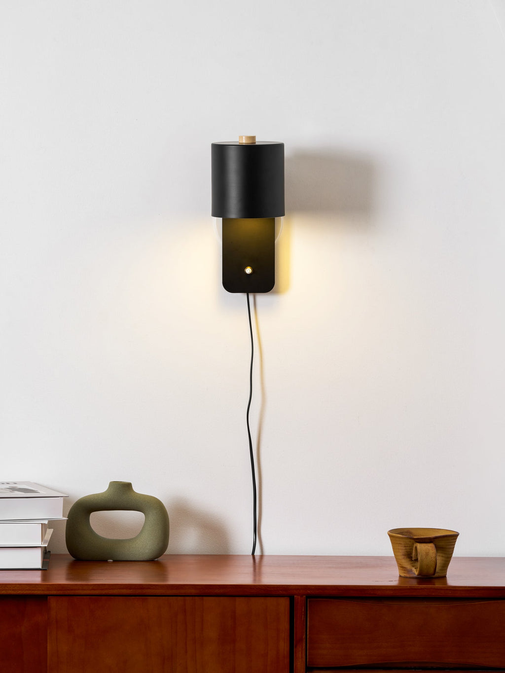 Minimalist metal cylinder wall lamp mounted beside a bed