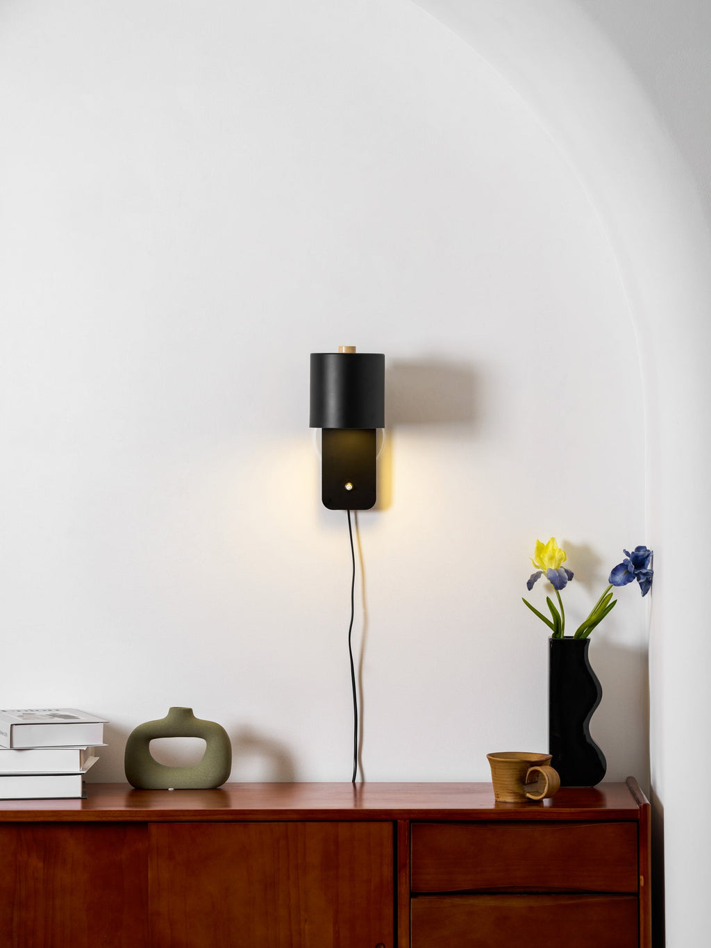 Cylinder wall lamp glowing warmly against a clean neutral wall