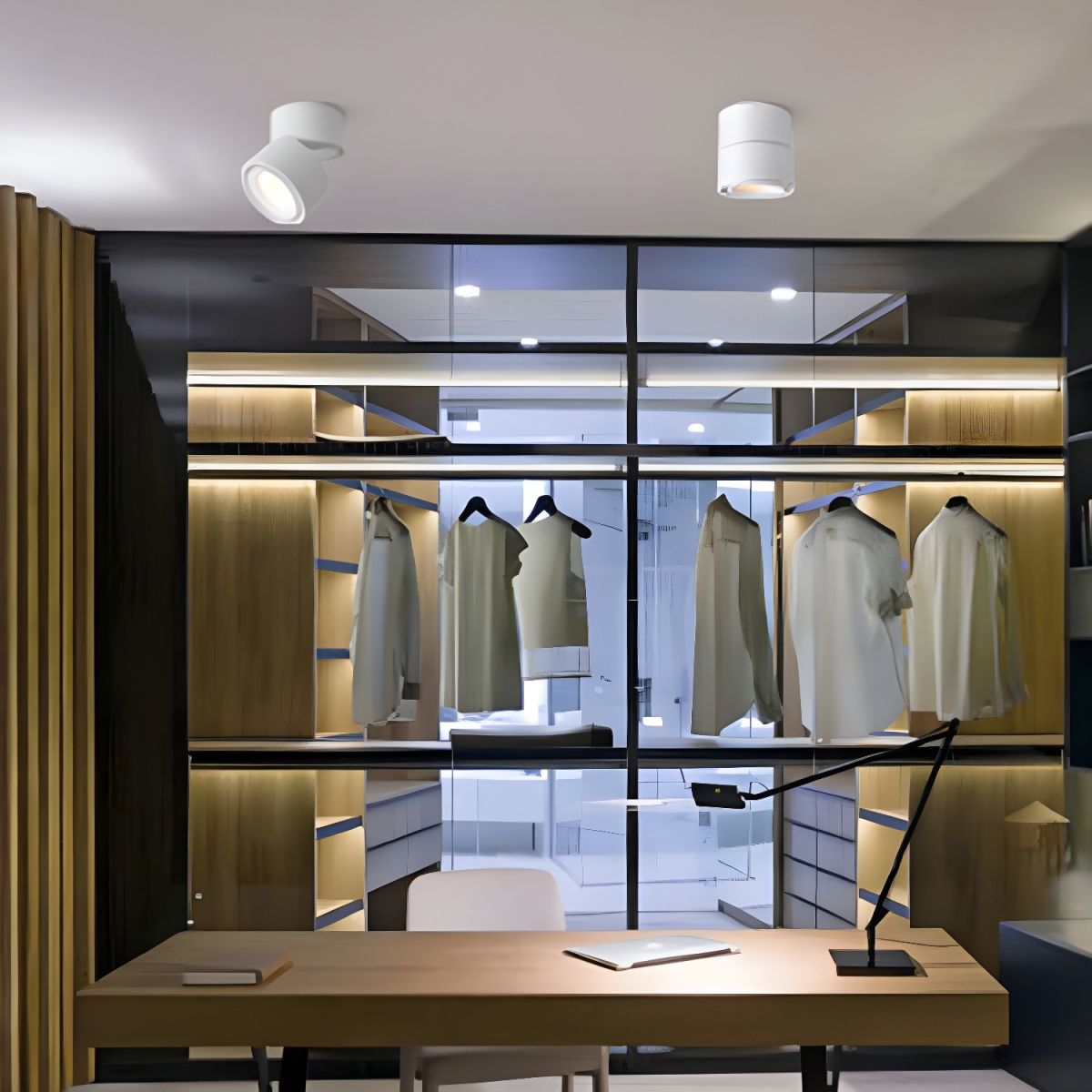 A single white Clérachic spotlight is mounted on the ceiling of a walk-in closet with hanging clothes.