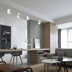 Several white Clérachic spotlights sit along a ceiling above an open lounge with a desk and armchair.