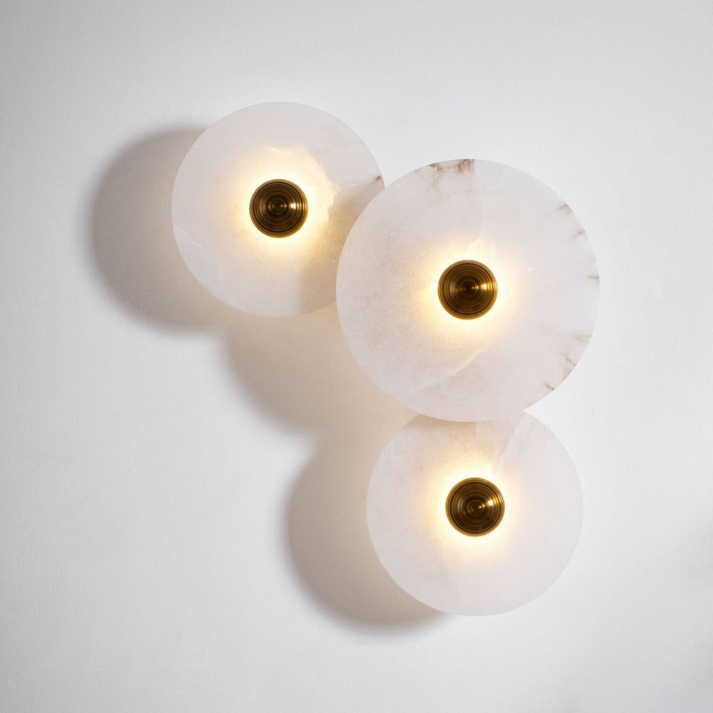 Three lit alabaster discs on a white wall, brass centres bright and shadows cast to the left.