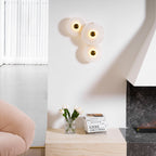 Three-disc cluster lit on a white living-room wall above tulips and a stack of books.