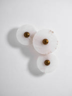 Three unlit alabaster discs on a white wall, cropped tall, brass centres and soft shadows.