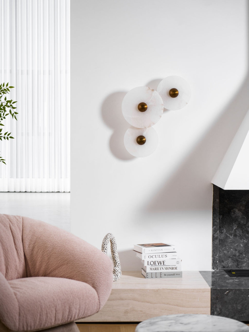 Three-disc alabaster cluster unlit on a white living-room wall beside a pink boucle chair.
