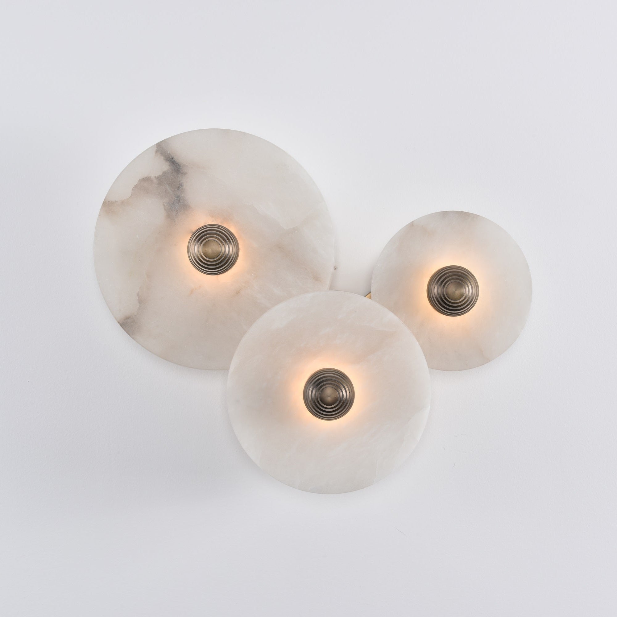 Three lit alabaster discs on white, the glow spreading evenly across each stone face.