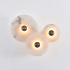 Three lit alabaster discs clustered on a pale grey wall, aged bronze centres and warm halos.