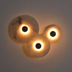 Three-disc cluster lit in a dim room, warm light washing up the grey wall behind the stone.