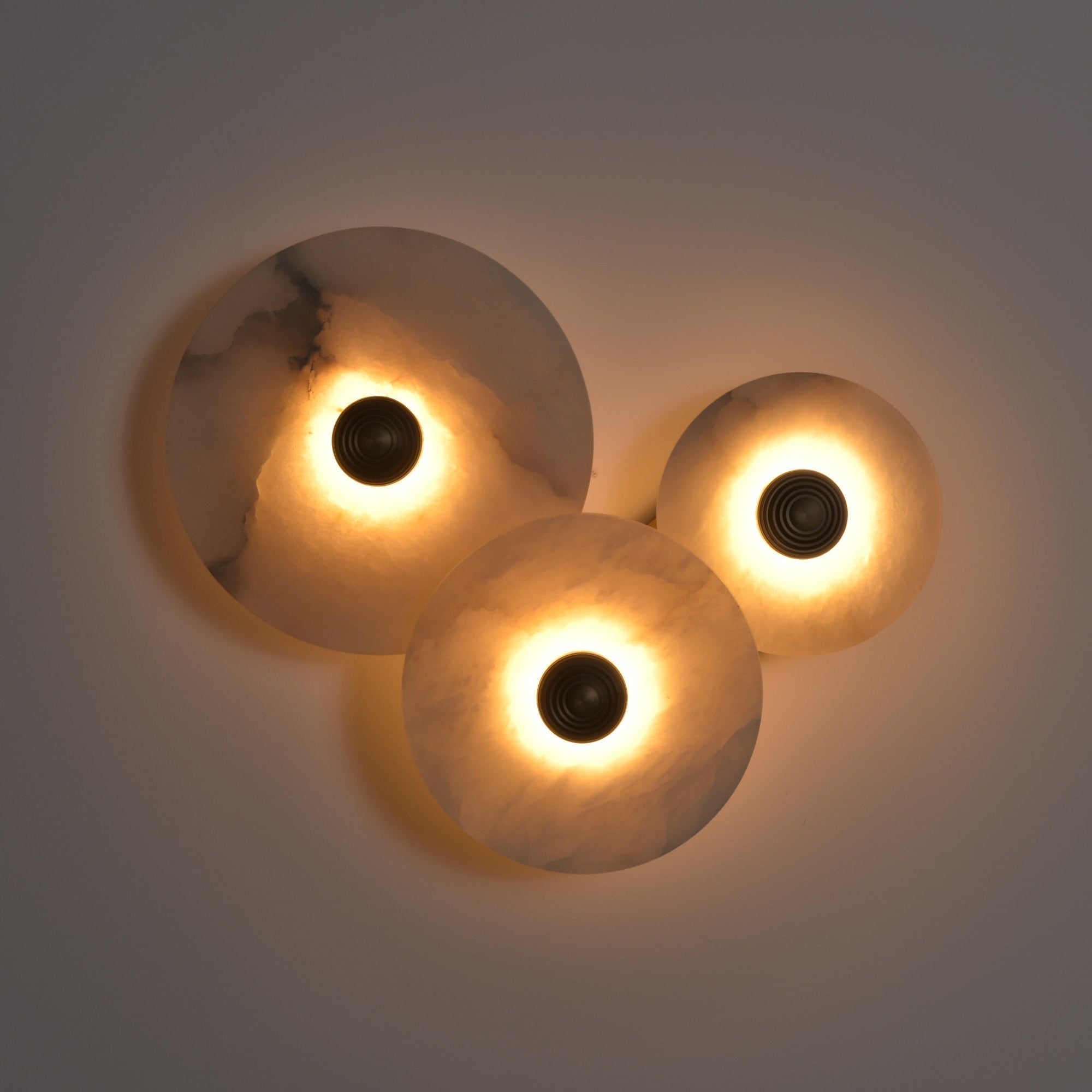Three-disc cluster lit in a dim room, warm light washing up the grey wall behind the stone.