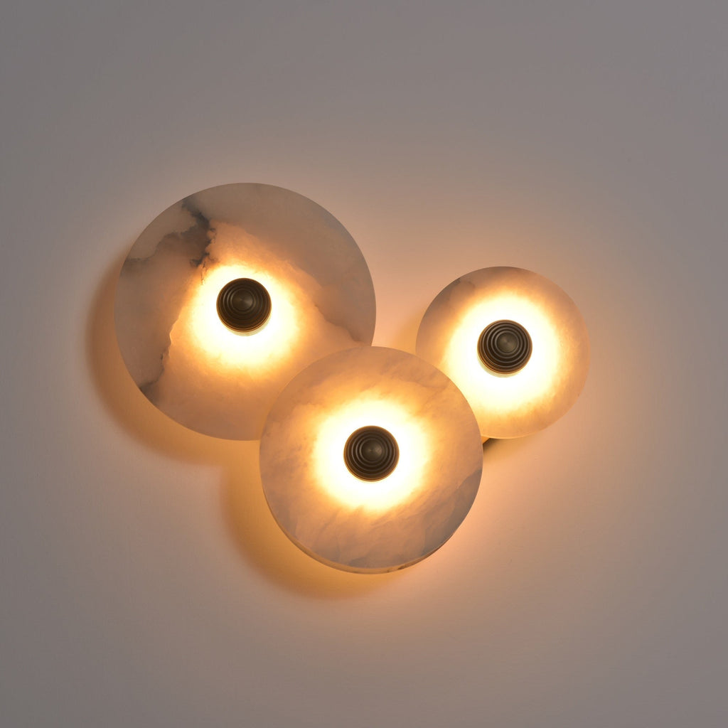 Three-disc alabaster cluster lit in a dim room, warm light pooling across the grey wall.
