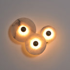 Three-disc alabaster cluster lit in a dim room, warm light pooling across the grey wall.