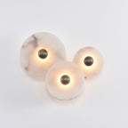 Three-disc cluster lit on a white wall, angled so the sawn edge of each stone disc is visible.