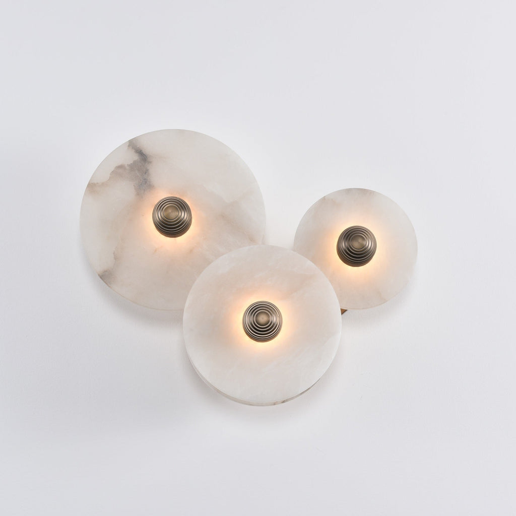 Three lit alabaster discs on a white wall, light kept low so the veining stays visible.