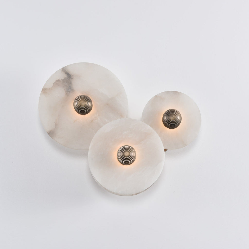Three-disc alabaster cluster with the light barely on, brass centres and pale stone in daylight.