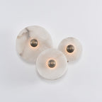 Three-disc alabaster cluster with the light barely on, brass centres and pale stone in daylight.