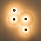 Four Clérachic sconces of different sizes lit together on a warm plaster wall, glowing behind each brass centre.