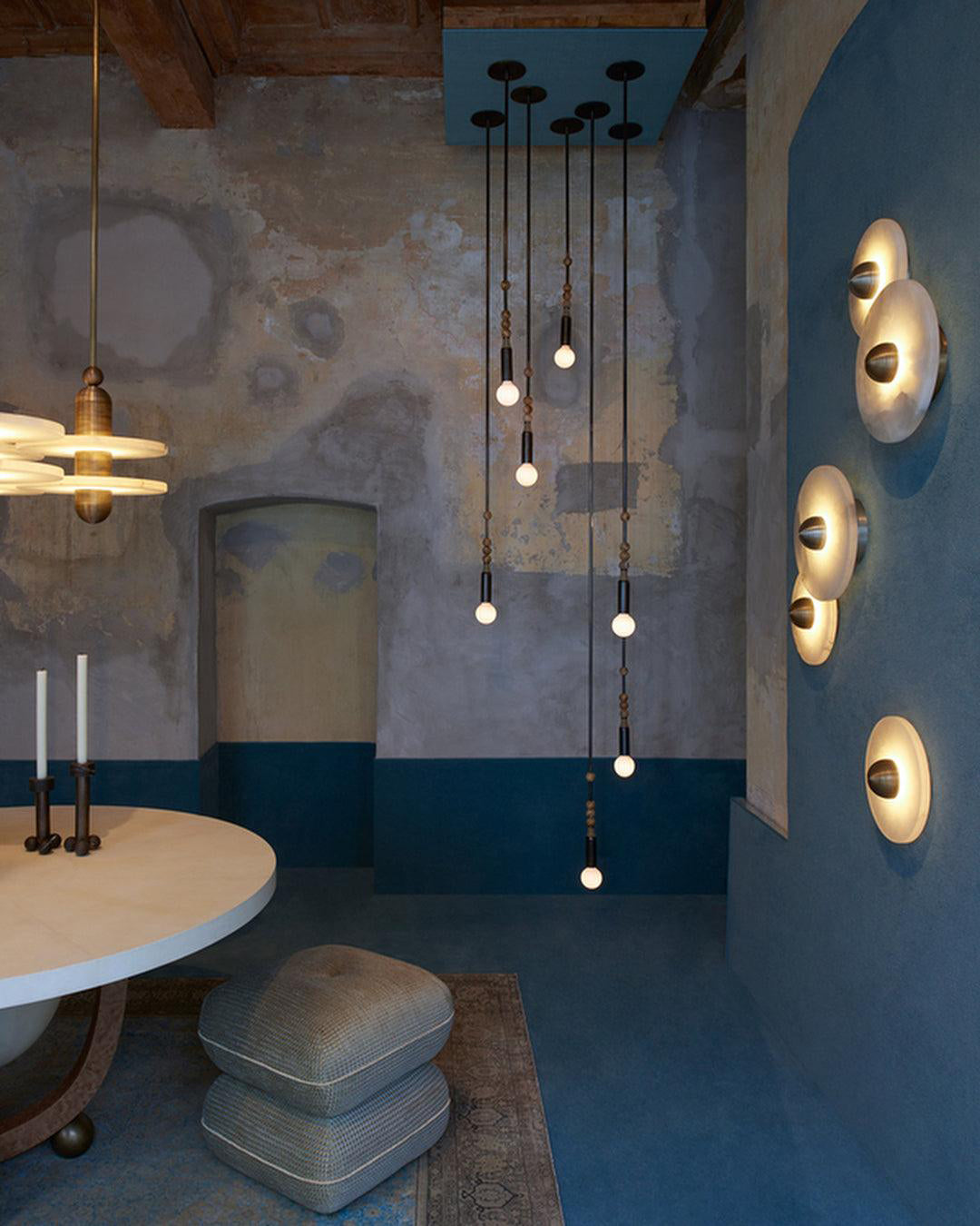 Clérachic five lit sconces on a deep blue wall to the right of a dining room with hanging bulb pendants.