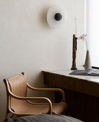 A Clérachic single sconce with a dark ribbed centre on a cream plaster wall above a marble desk and leather chair.