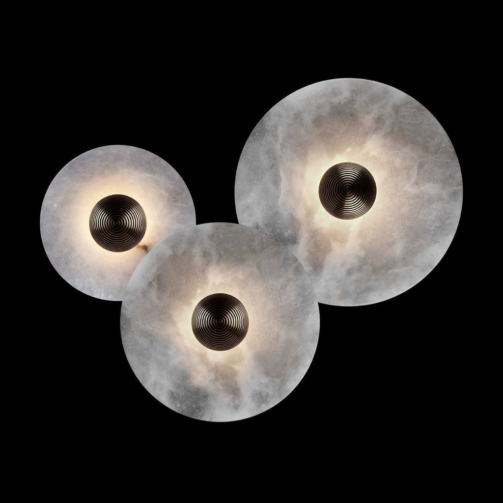 Three Clérachic lit sconces in different sizes photographed against black, the alabaster glowing around bronze centres.