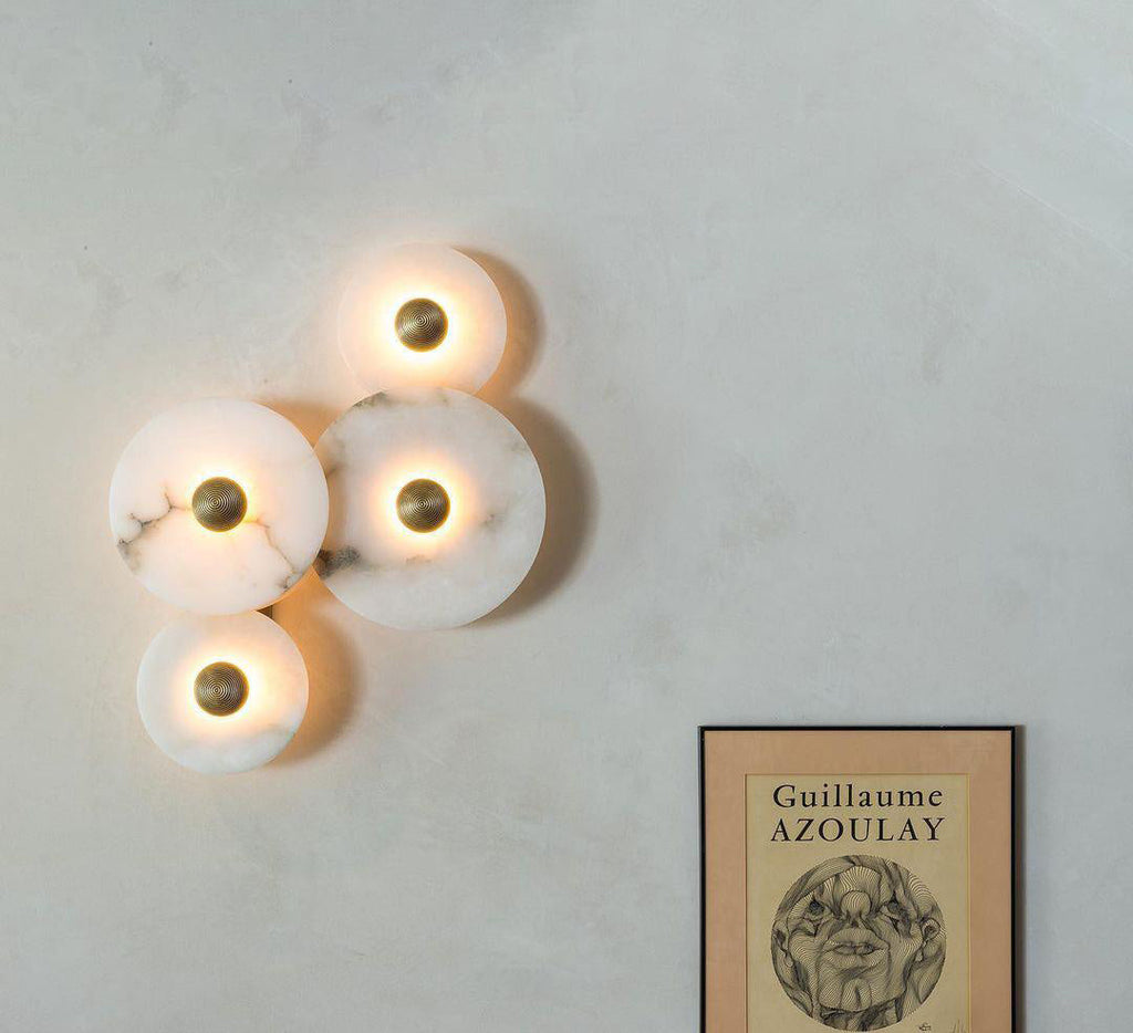 Four Clérachic lit sconces clustered in a diamond on a pale plaster wall beside a framed print.